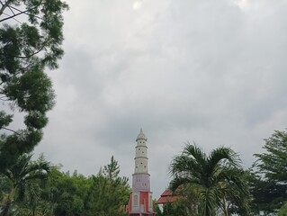 Obraz premium Tall White Tower with Red and Purple Accents Surrounded by Trees
