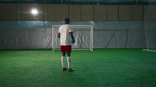 Black soccer player exercising penalty in training hall, scoring goal, back view