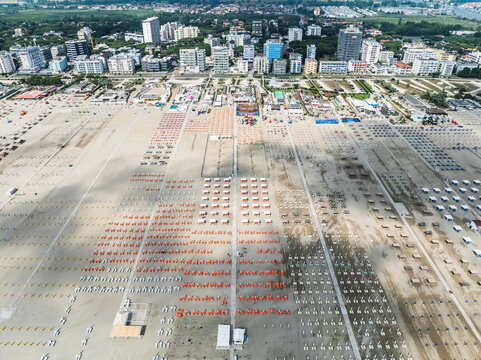 Aerial images of beach full of lounges in perfect arrangement with town in the background. Lido degli Esters, Italy