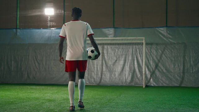 African american player in sports uniform stands in front of the goal with a soccer ball. Man wearing a jersey, shorts, and cleats is standing ready to take a shot. Sport, soccer, football concept.