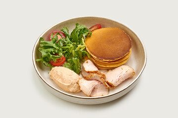 A classic American breakfast of pancakes, ham, and a fresh salad. The pancakes are golden brown and fluffy, and the salad is made with fresh greens and tomatoes.