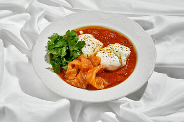 A classic Shakshuka dish with poached eggs, a flavorful tomato sauce, and fresh herbs. The dish is served with smoked salmon and is a popular Middle Eastern breakfast.