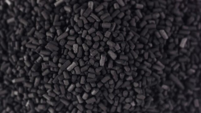 A close-up shot of active carbon reveals its granular, porous texture with tiny, dark particles. The footage emphasizes the intricate surface details.