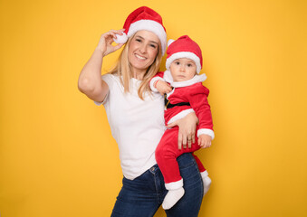 Fototapeta premium Portrait of a mother with little daughter wearing santa hat isolated on yellow background.