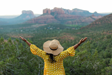 Woman in a yellow polka dot dress, wearing a hat, gazing at red rocks.