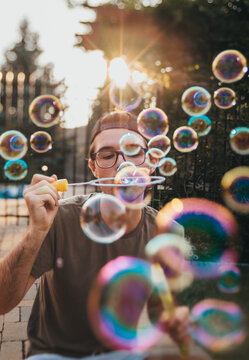 Older teen boy blowing soap bubbles outdoors on sunny day.