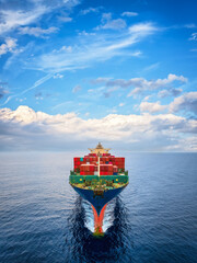 Aerial front view of a large container cargo ship sailing over the ocean with speed with the sky as...