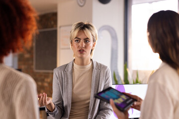 At office, discussing creative writing business, woman talking with colleagues holding tablet