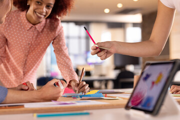 Collaborating on creative writing project, multiracial women using tablet and markers in office