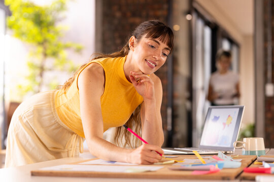At office, Writing on sticky notes, woman brainstorming ideas in creative workspace with laptop