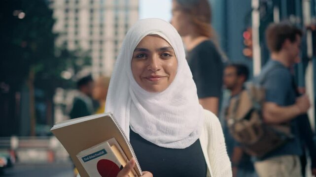 Arab Female Student Wearing a White Hijab Standing on a Crowded Street, Holding Textbooks Close to Her Chest. Urban City Scene Represents Her Ambition and Commitment to Academic and Work Success