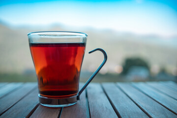 A warm cup of tea rests on a wooden table overlooking a serene mountain landscape during daylight hours
