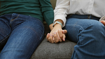 A woman and a man holding hands, showcasing intimacy and connection in a comfortable home setting.