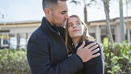 Affectionate couple embracing in a sunny urban park with greenery, expressing love and companionship.