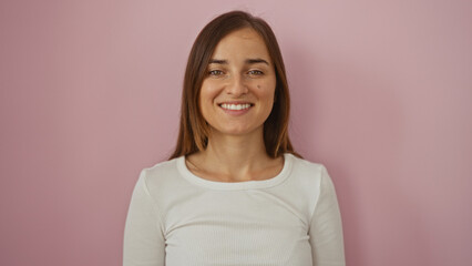 Fototapeta premium Smiling young woman with long blonde hair stands isolated over a pink background, creating an attractive and cheerful portrait.