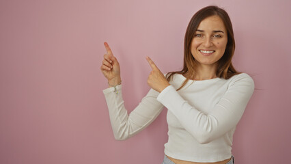 Young attractive blonde woman pointing up with both hands while smiling, against an isolated pink background wall.