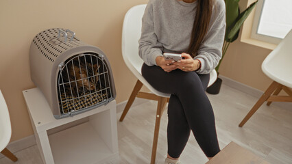 A woman and her cat wait patiently in a veterinary clinic's waiting room, with the woman using her...