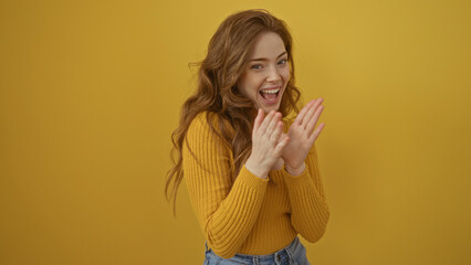 A young blonde woman is clapping and smiling joyfully against an isolated yellow background wall.