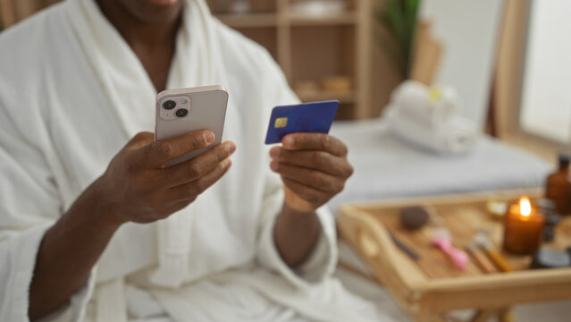 Young man at spa using phone and credit card in relaxing wellness room