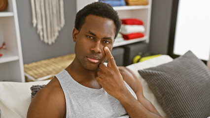 A thoughtful young african american man in a casual indoor bedroom setting touching his face.