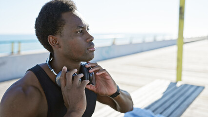 Thoughtful young african american man with headphones enjoying the peaceful ocean view at the beach.