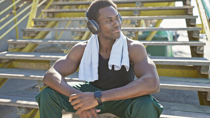Athletic young african american man with headphones resting on urban stairs outdoors, exuding a sense of health and wellbeing.