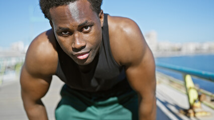 Young african american man in workout gear resting near the seaside with a blurred beach backdrop.