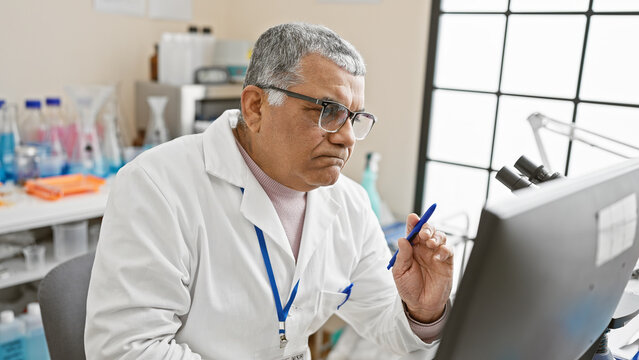 Mature man scientist in lab coat analyzing data on computer screen in laboratory setting