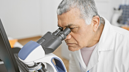 Middle-aged man in lab examining samples under microscope in healthcare setting.