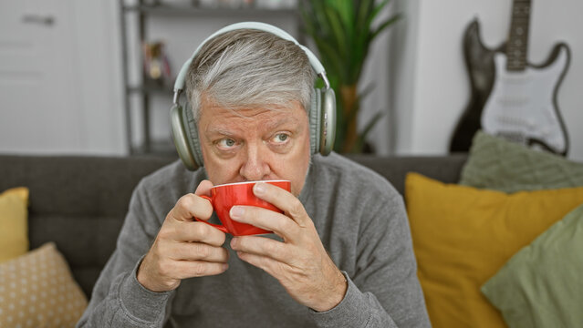 A middle-aged man enjoys coffee at home with headphones in a cozy living room setting, exuding relaxation and comfort.