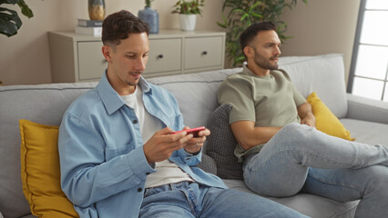 Obraz premium Men relaxing together in a comfortable living room setting, depicting a modern and cozy home interior with two individuals enjoying each other's company on a sofa.