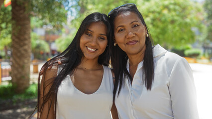 Naklejka premium Mother and daughter embracing in a sunny urban park, showcasing family love and happiness outdoors in the city surrounded by greenery and smiles.