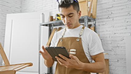 Hispanic carpenter using tablet in a well-equipped workshop, embodying expertise and modern craft.