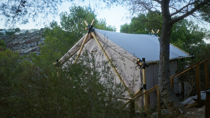 A rustic tent set up in a scenic african wilderness, surrounded by lush trees and rocky hills,...