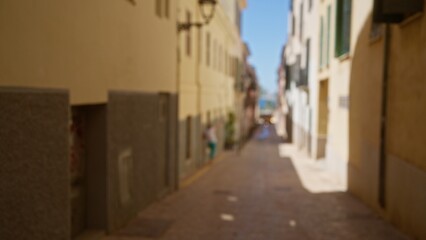 Fototapeta premium Blurred street in mallorca featuring a defocused person walking in an outdoor setting under bright sunlight.