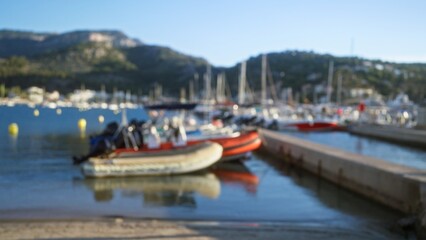 Obraz premium Blurred image of boats docked at a marina with mountains in the background, emphasizing a peaceful harbor setting with soft focus.