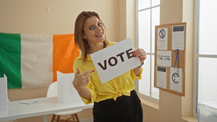 A young attractive blonde woman in an indoor electoral college room in ireland holds a vote sign...