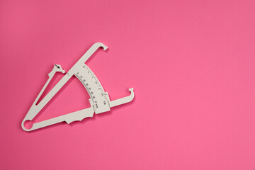 Plastic body fat caliper on pink background, top view. Space for text