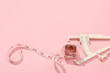 Body fat caliper and measuring tape on pink background. Space for text