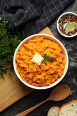 Delicious mashed sweet potatoes with butter, spices, bread and spoon on dark table, top view