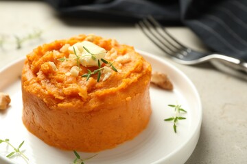 Plate with tasty mashed sweet potato, butter, thyme and walnuts on grey textured table, closeup