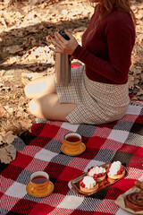 Woman holding a thermos. Fall picnic ideas in the park with tarts, tea on the plaid. Cozy autumn breakfast