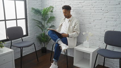 Young african american man with a beard reading a clipboard while seated in an indoor waiting room...