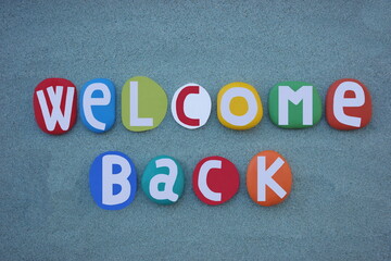 Welcome back, creative slogan composed with hand painted multi colored stone letters over green sand