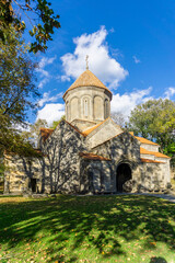 Manglisi Sioni Cathedral in the shade of trees. Central arched entrance. Green lawn, bright sky