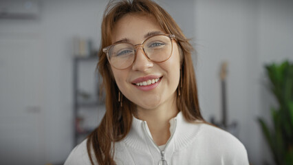 A smiling caucasian woman wearing glasses in a casual indoor setting, exuding a sense of warmth and approachability.