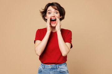 Young excited happy woman wear red t-shirt casual clothes scream sharing hot news about sales discount with hands near mouth isolated on plain pastel light beige background studio. Lifestyle concept.