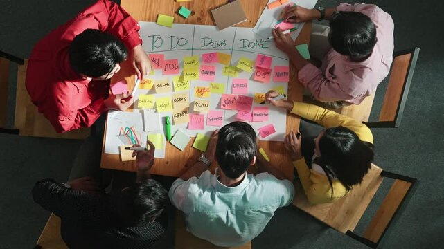 Top view of people writing and making scrum task board while writing marketing and planning strategy at colorful sticky notes. Smart team manage work performance by using kanaban board. Convocation.