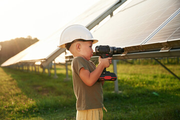 Doing repairs by using drill. Little boy is with solar panels outdoors