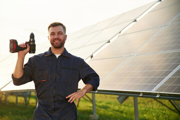 Ready for the work. With drill. Man is near solar panels outdoors at daytime